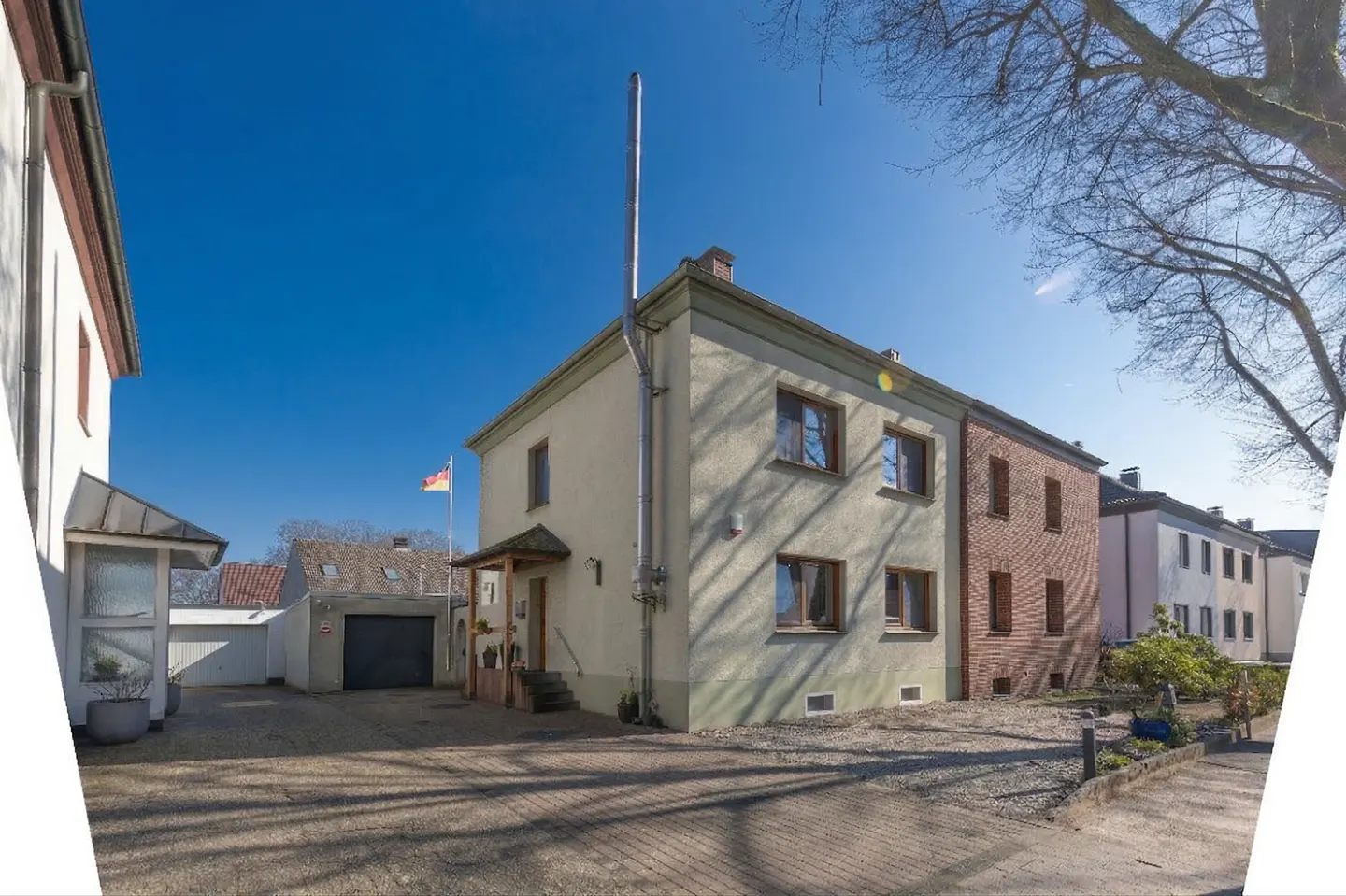 Two-story house with a tall chimney, a German flag, and a garage on a sunny day.