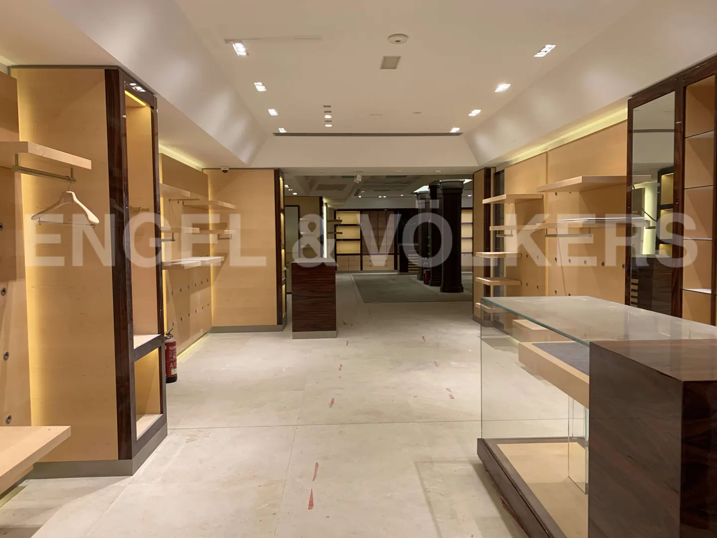 Empty retail store interior with light wood shelving, dark wood accents, recessed lighting, and a glass display counter.