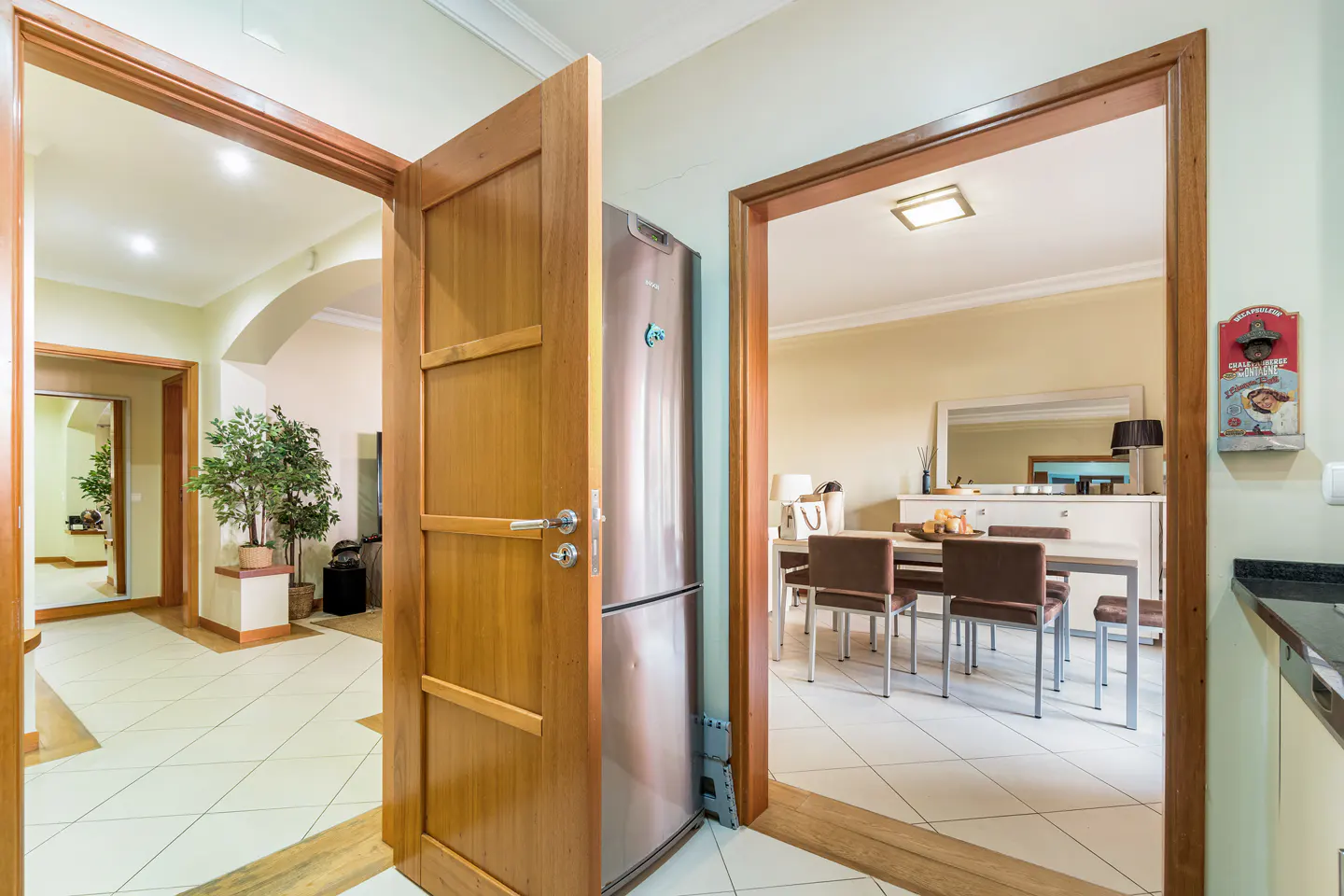Interior view of a home with open wood doors, a stainless steel refrigerator, and a dining room with table and chairs.