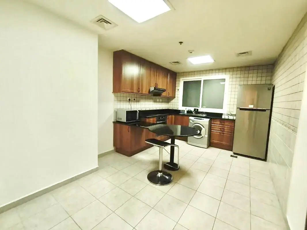 A kitchen with brown cabinets, stainless steel appliances, and a black table with a stool.