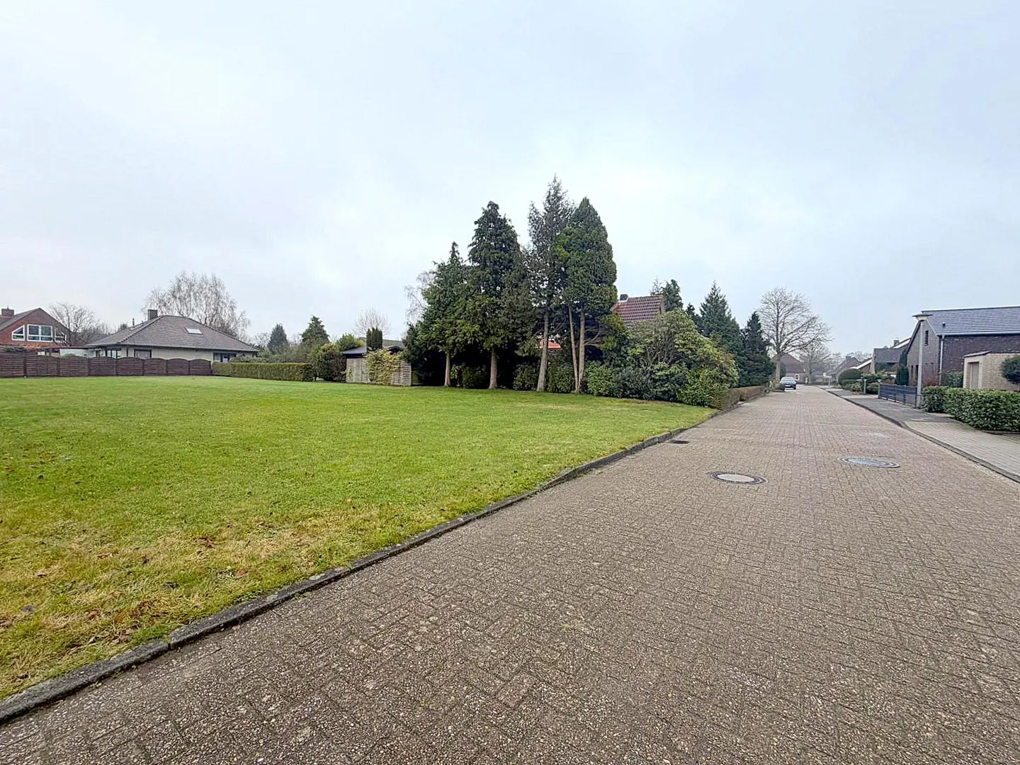 A street view of a green lawn and houses under a cloudy sky.