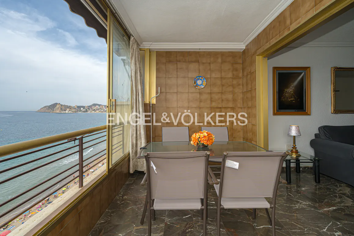 Balcony view of a beach apartment with a glass table, chairs, and ocean view. Engel & Völkers logo is visible.