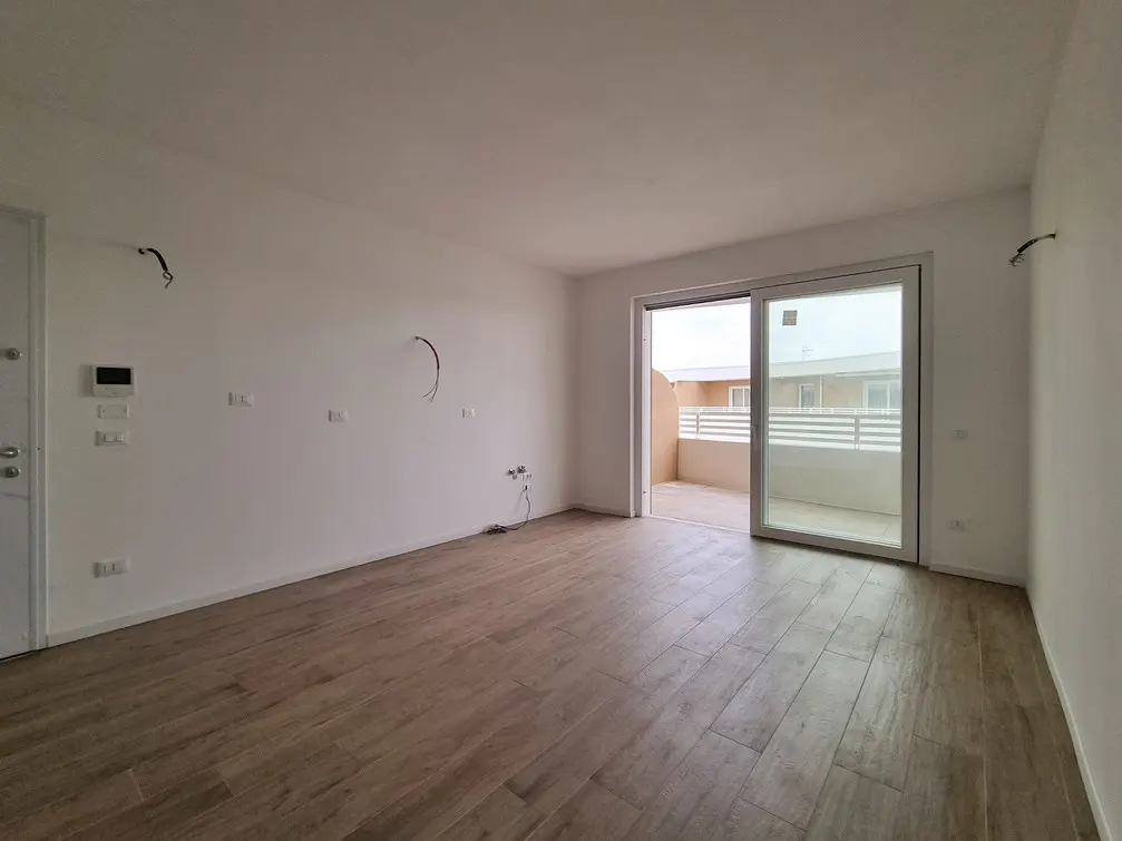 Empty room with light wood floors, white walls, and sliding glass doors to a balcony. Electrical wiring is exposed on the walls.