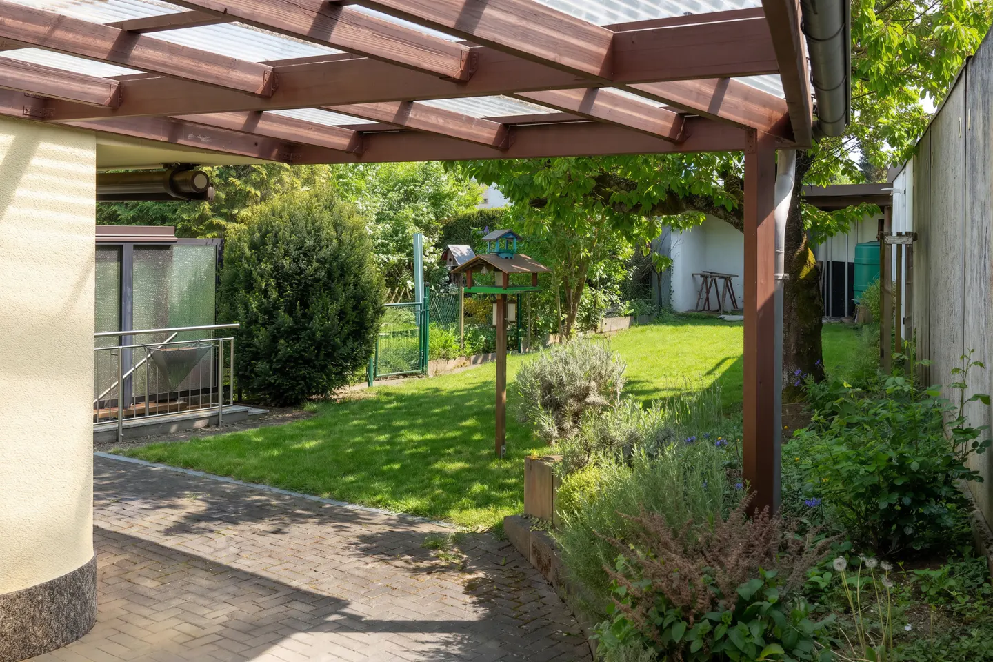 A backyard with a brown pergola, green grass, and a birdhouse.