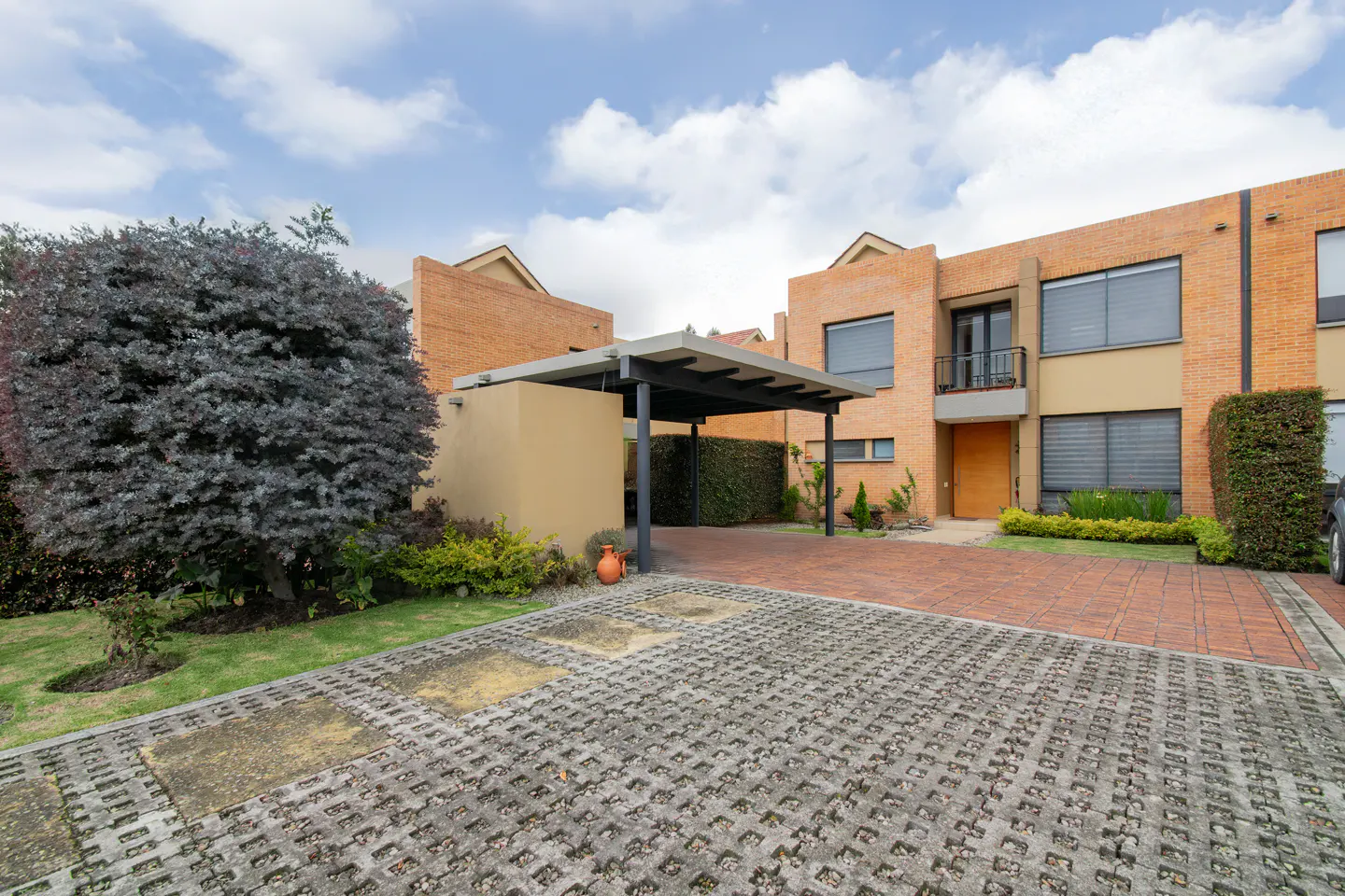 Brick townhouse with a carport and a gray paver driveway on a cloudy day.
