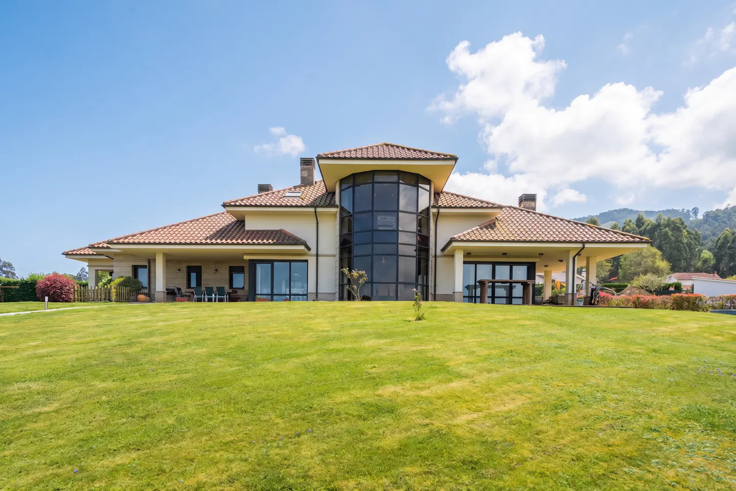 Beige house with a red tile roof and a large black glass window on a green lawn under a blue sky.