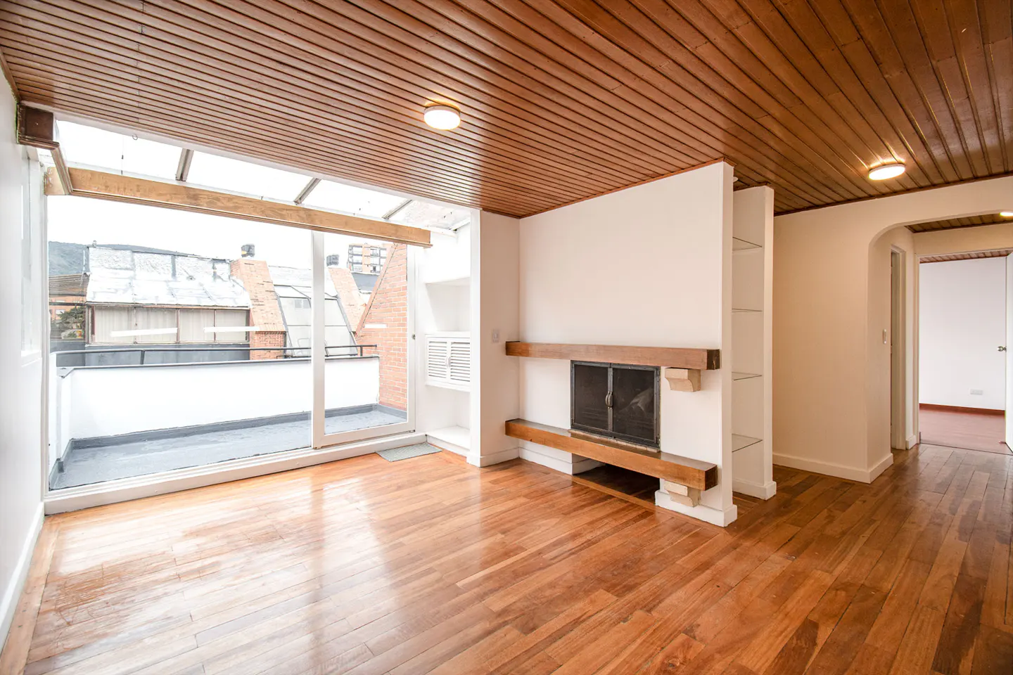 Living room with wood-paneled ceiling, hardwood floors, a fireplace, and large sliding glass doors leading to a balcony.
