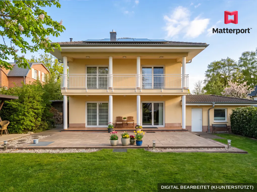 Two-story yellow house with white columns and balcony, a patio with potted flowers, and a green lawn.