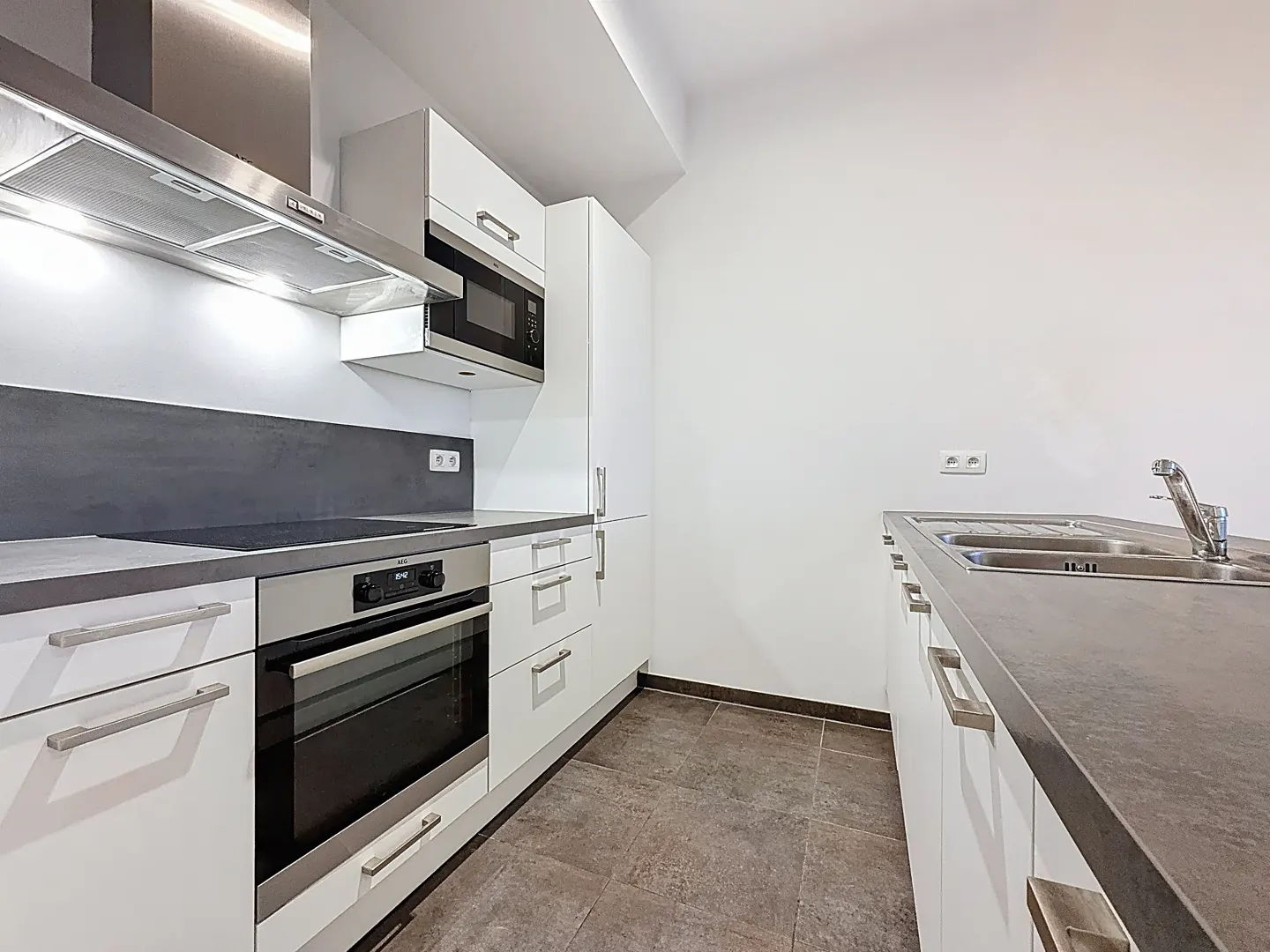 Modern galley kitchen with white cabinets, dark gray countertops, stainless steel appliances, and tiled flooring.