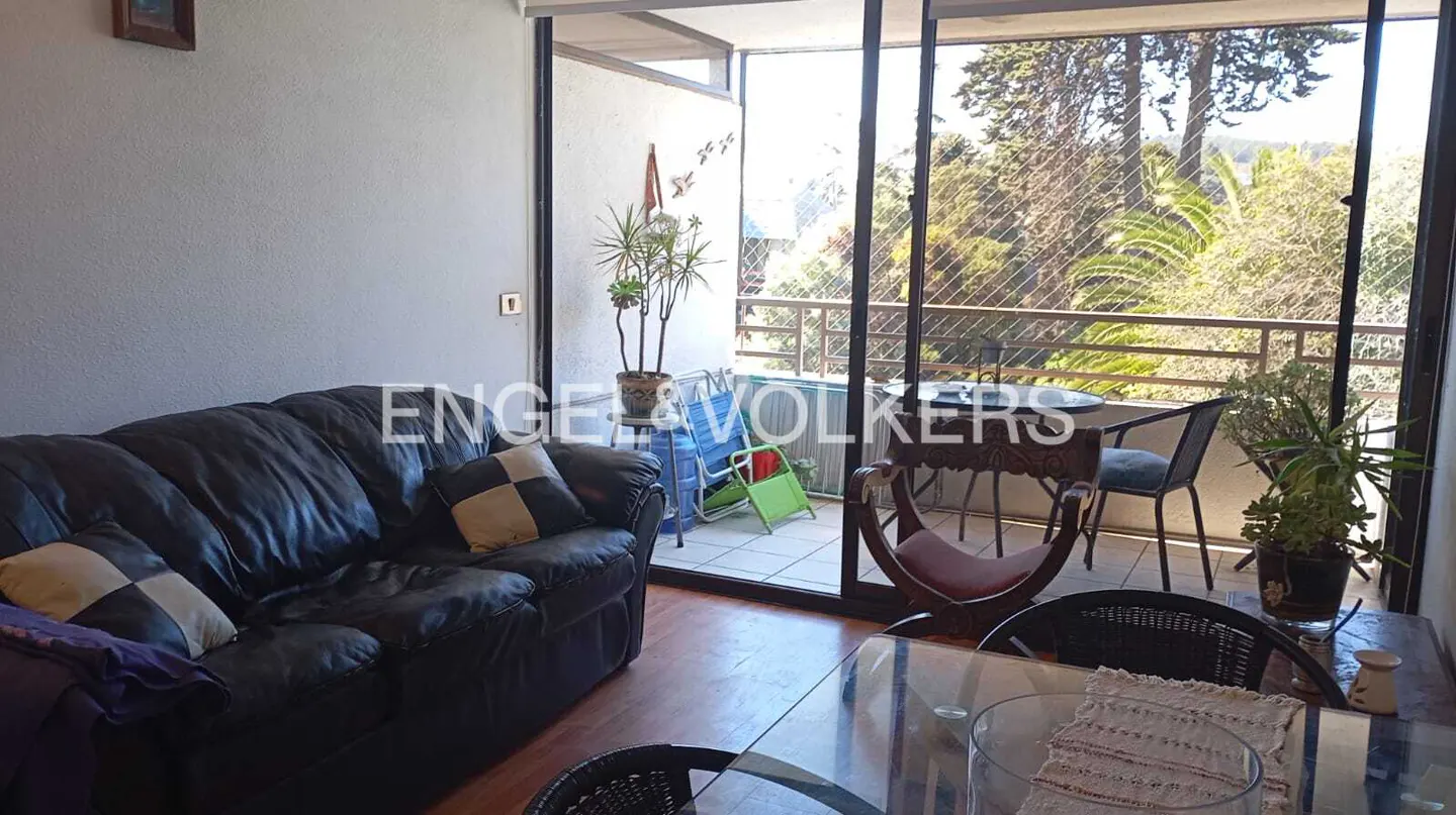 Living room with a black leather sofa, a glass table, and a balcony with a view of trees.