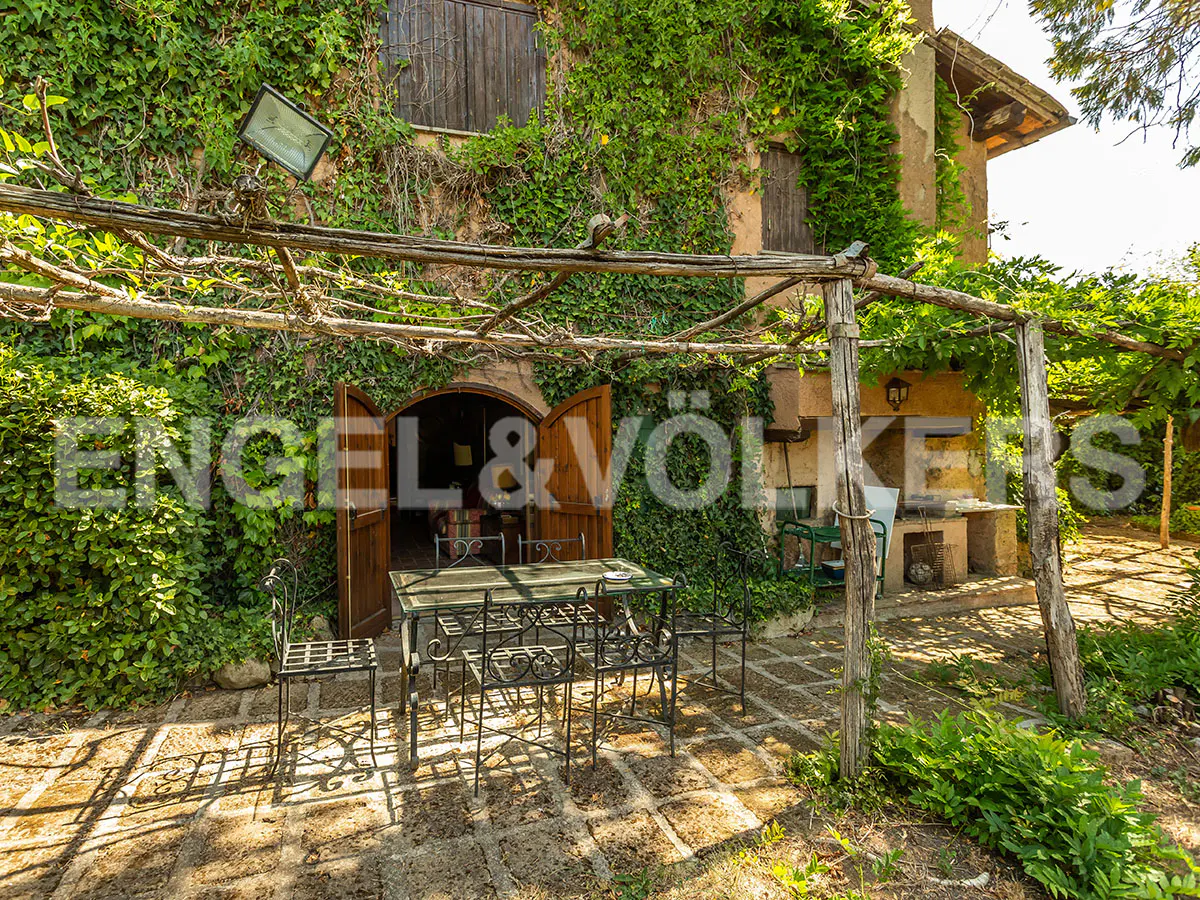 Outdoor patio with stone pavers, table, and chairs under a wooden pergola. The building is covered in ivy.