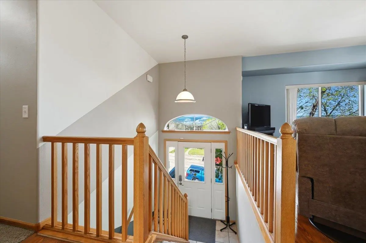 Interior view from the top of wooden stairs looking down to a white front door with an arched window above.