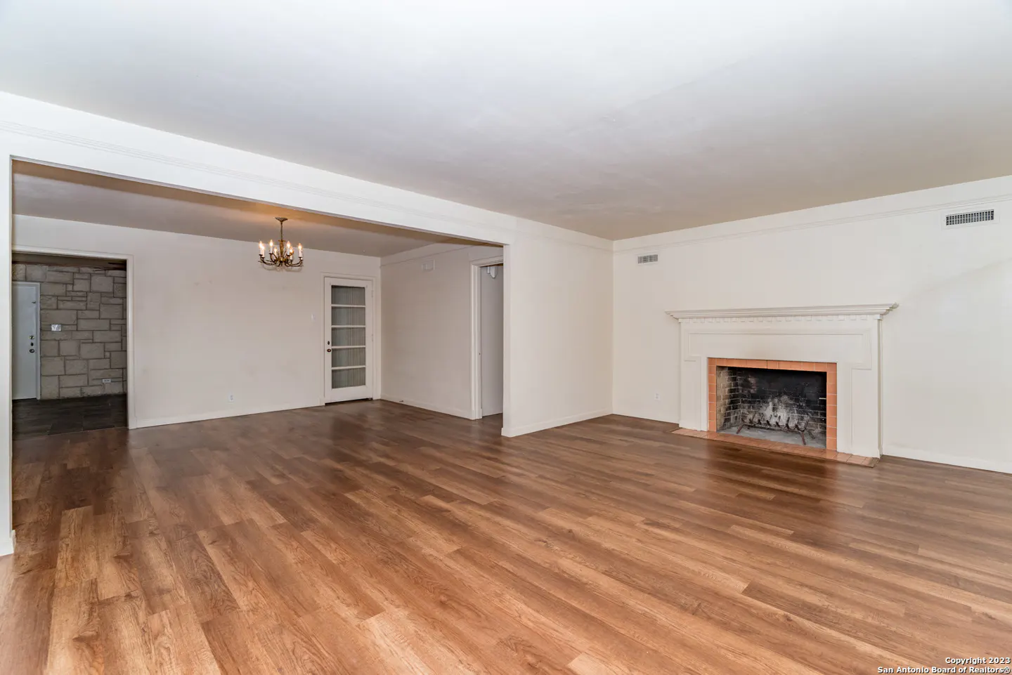 Spacious living room with wood-look floors, a white fireplace, and a view into a room with a stone wall and chandelier.