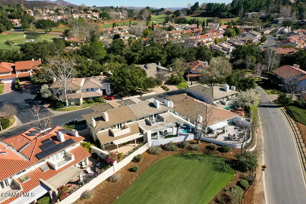 Aerial view of a suburban neighborhood with multi-story homes, terracotta roofs, and a green golf course in the foreground.