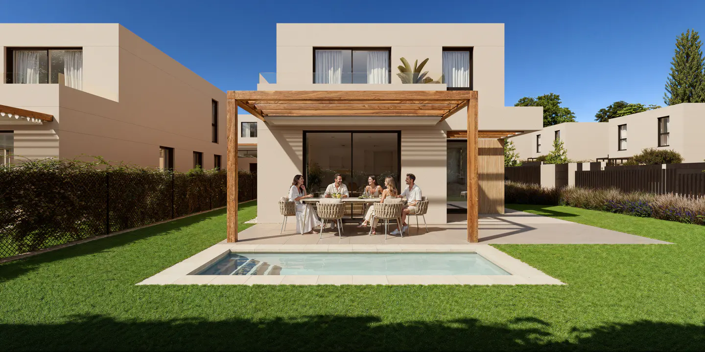 A modern, beige house with a wooden pergola over a patio where six people sit at a table near a small, rectangular pool in a green lawn.