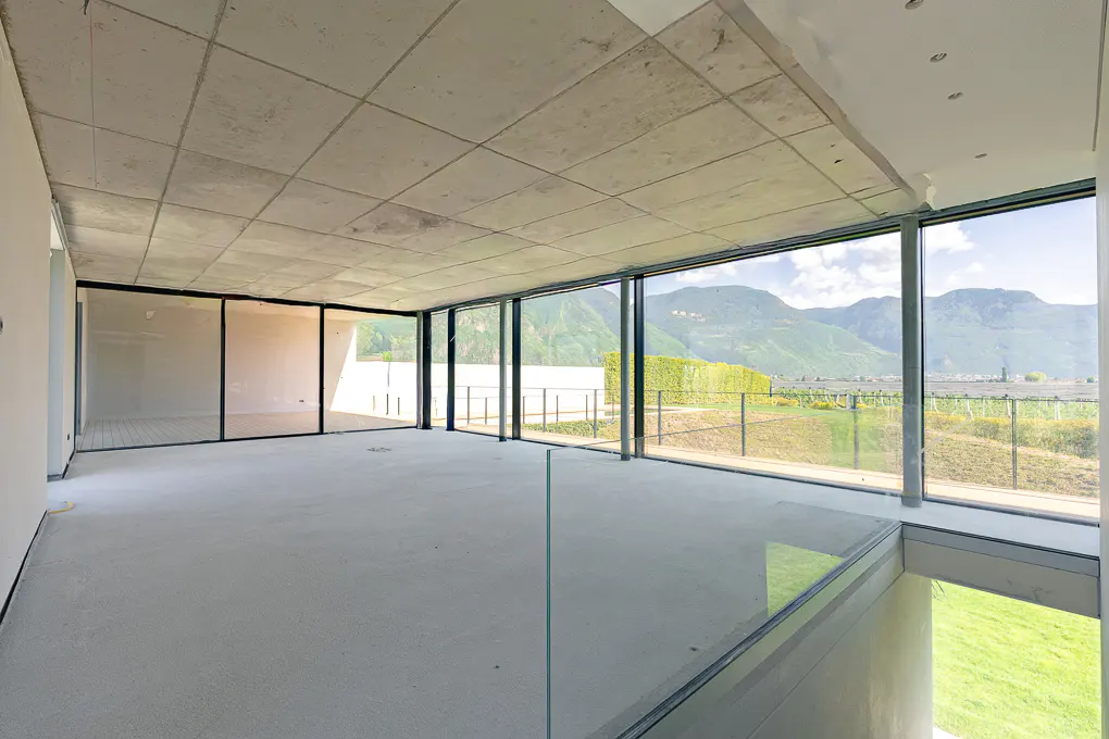 Unfinished room with concrete ceiling, floor, and large windows. Outside, green hills and mountains are visible.