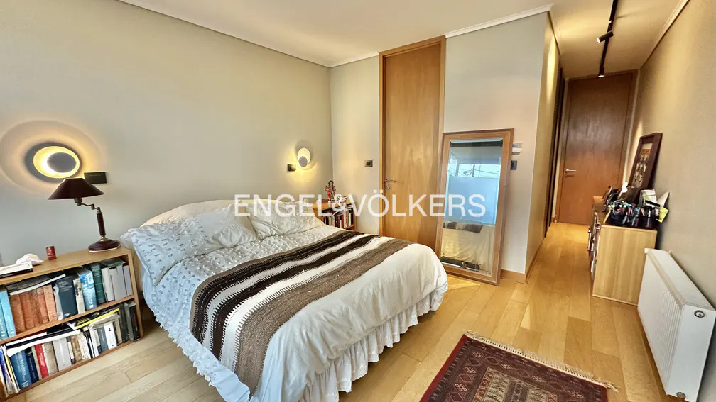 Bedroom with a white bed, brown blanket, wooden floors, a mirror, and a bookshelf.