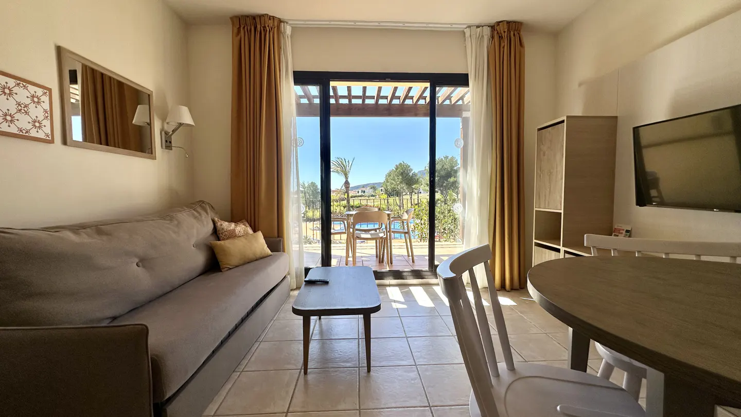 Living room with a gray sofa, wood table, and a view of a patio with a pool. Curtains are gold and white.