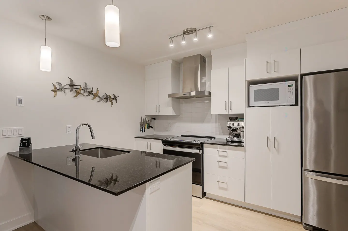 Bright kitchen with white cabinets, stainless steel appliances, and a black granite countertop island with a sink.