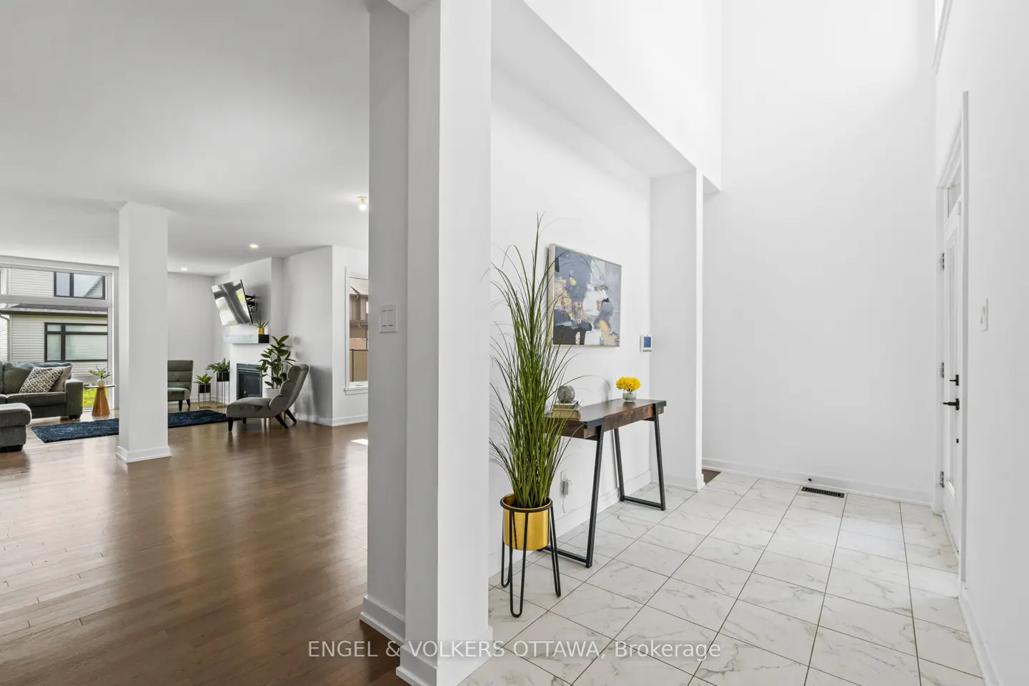 Bright foyer with white walls, marble tile floor, and a dark wood console table with a plant. Living room with hardwood floors in the background.