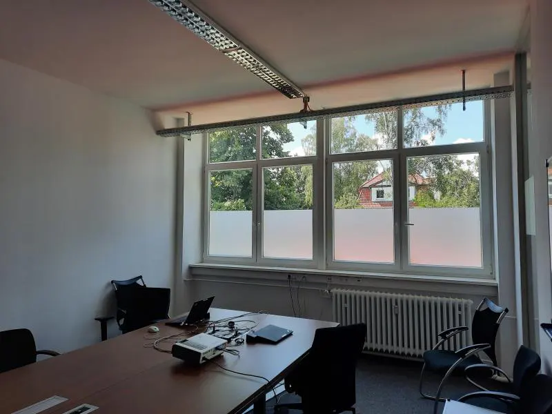 A conference room with a long brown table, black chairs, a projector, and a large window with frosted glass.