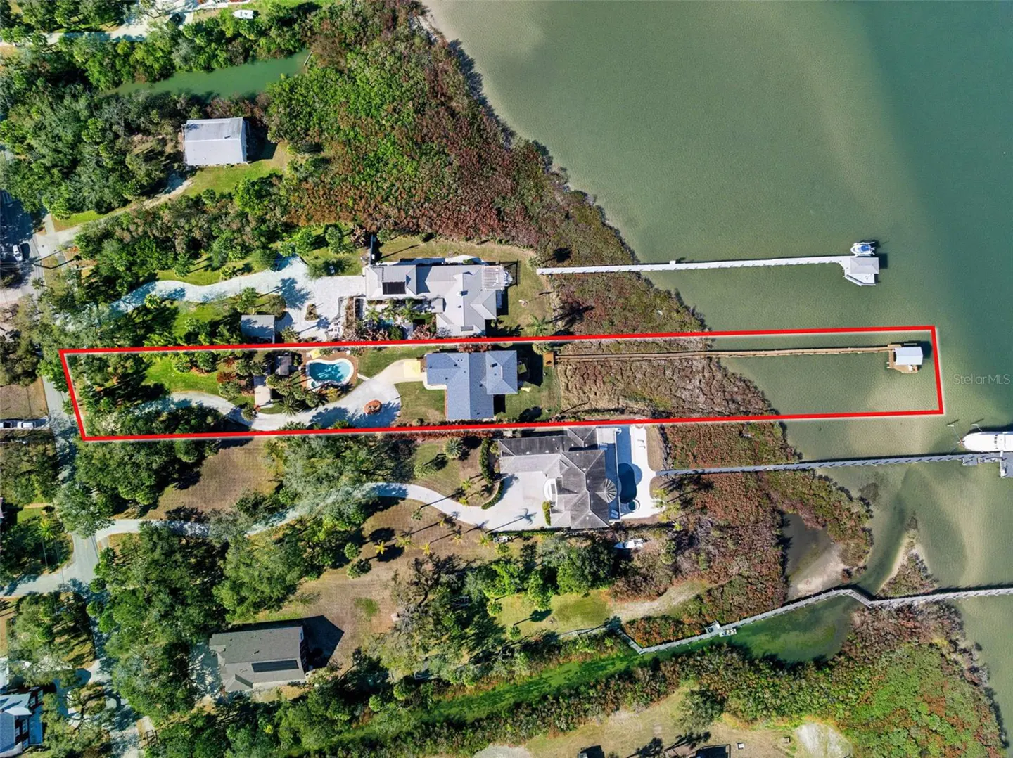 Aerial view of a waterfront property with a red outline, featuring a house, pool, dock, and boat lift.