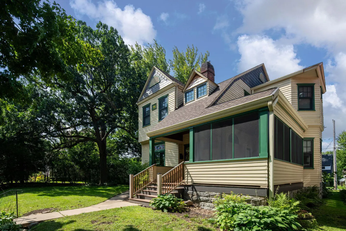 Exterior view of a two-story house with a screened porch, light yellow siding, green trim, and a brown shingle roof.