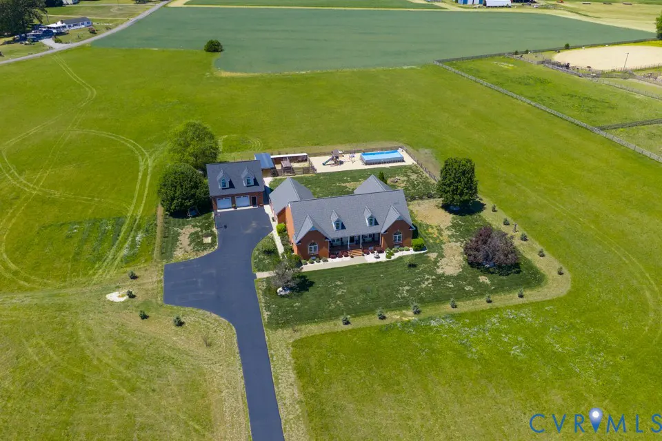 Aerial view of a red brick house with a gray roof, a pool, and a playground surrounded by a large green lawn.