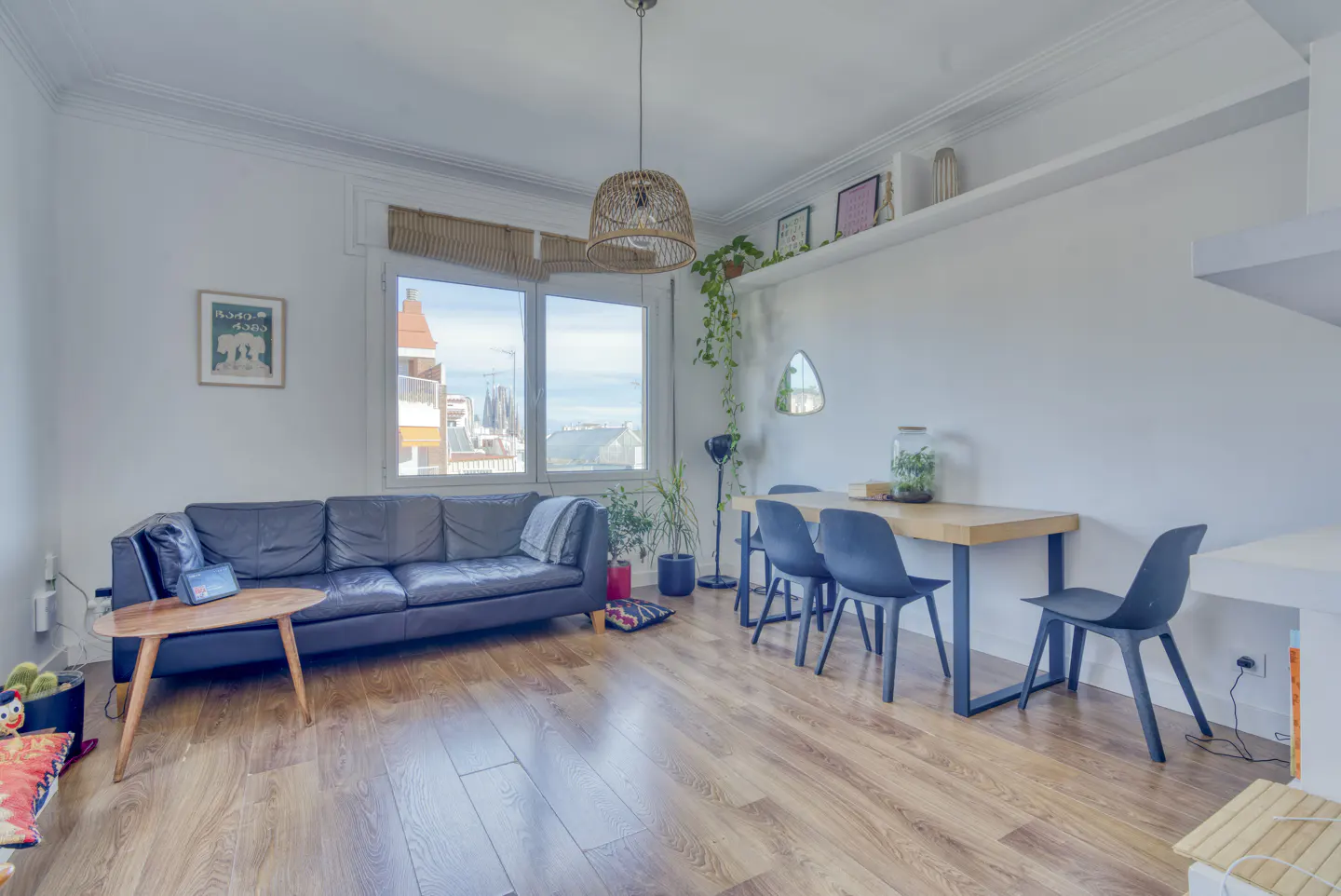 Bright living room with wood floors, a gray sofa, a wood table with black chairs, and a window with a city view.