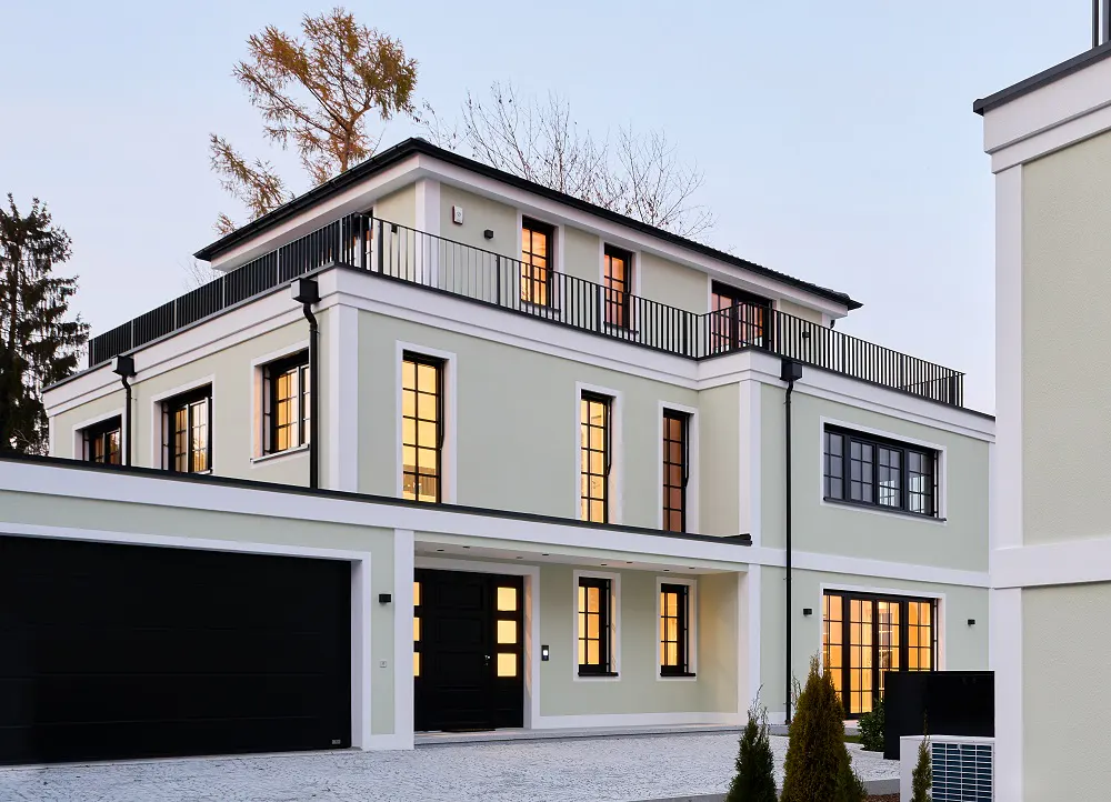 Two-story light green house with black trim, a black garage door, and a black railing on the roof.