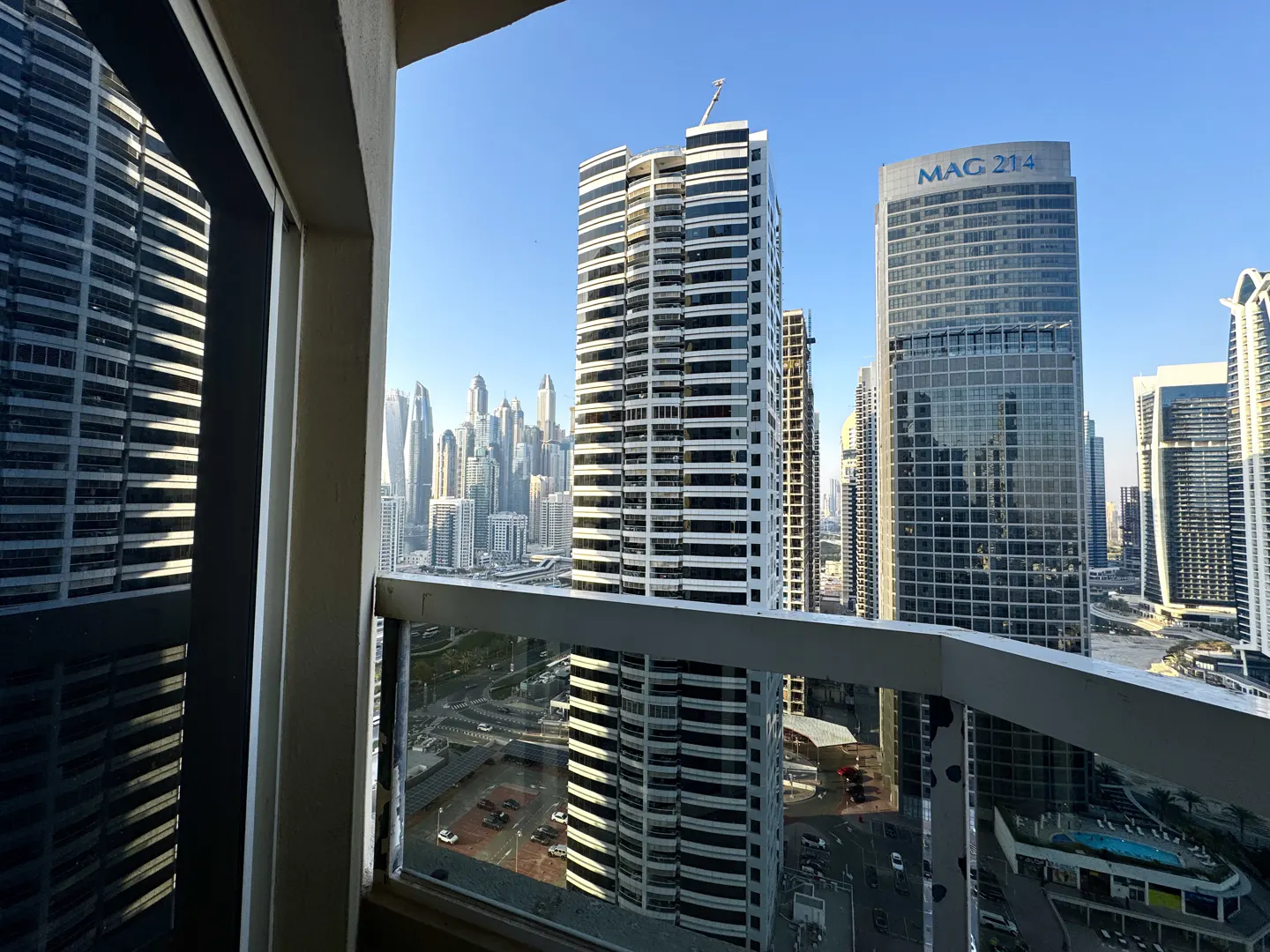 View from a balcony overlooking Dubai's skyline. Tall buildings and roads are visible. The sky is blue.