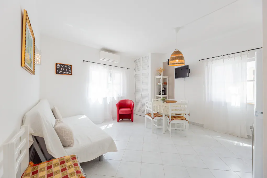 Bright living room with white tile floors, a white sofa, a red armchair, and a dining set under a woven pendant light.