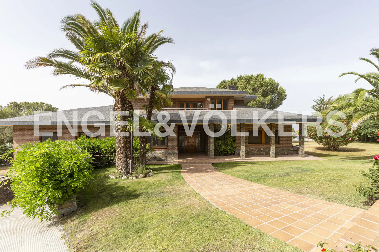 Exterior view of a two-story brick house with a tile walkway, palm trees, and green lawn.