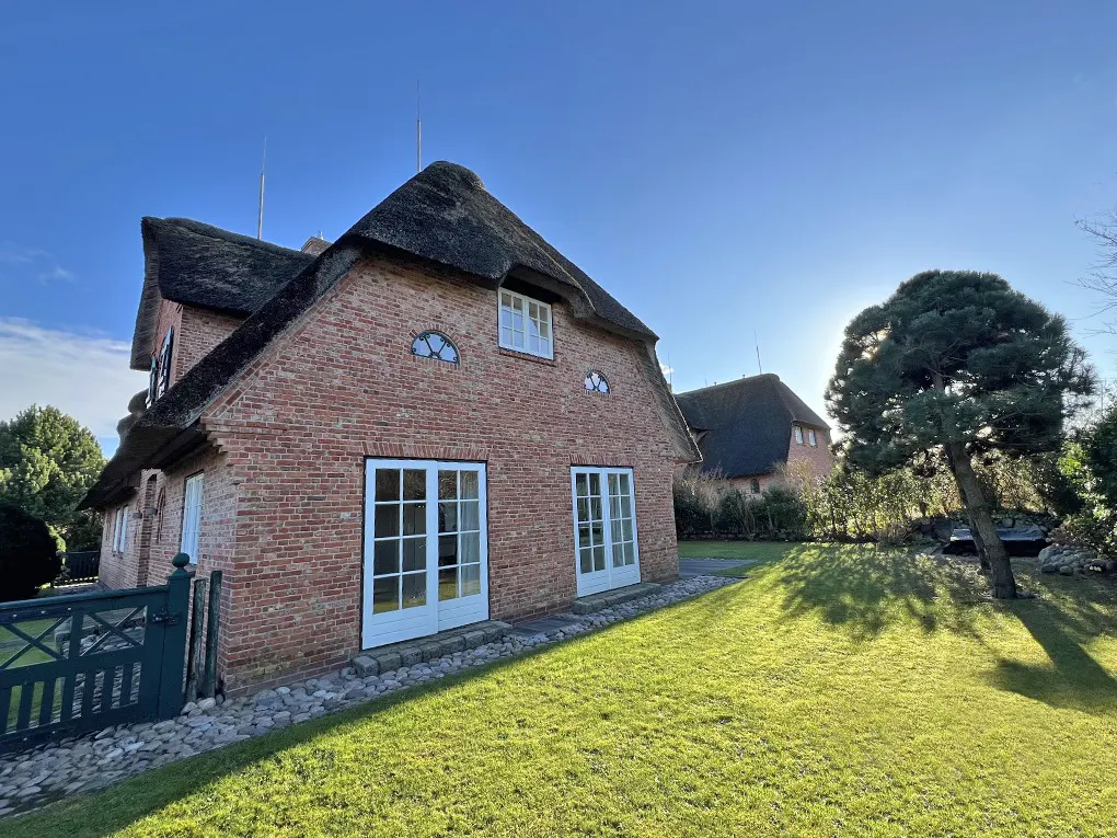 Brick house with a thatched roof and white-framed windows, set on a green lawn under a blue sky.