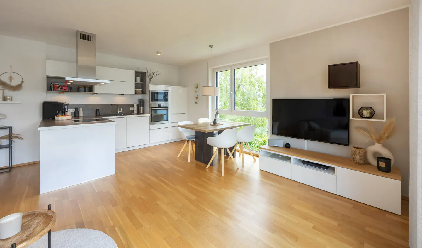 Bright, open-concept apartment with wood floors. White kitchen with island, dining table with four chairs, and a TV with a white media console.
