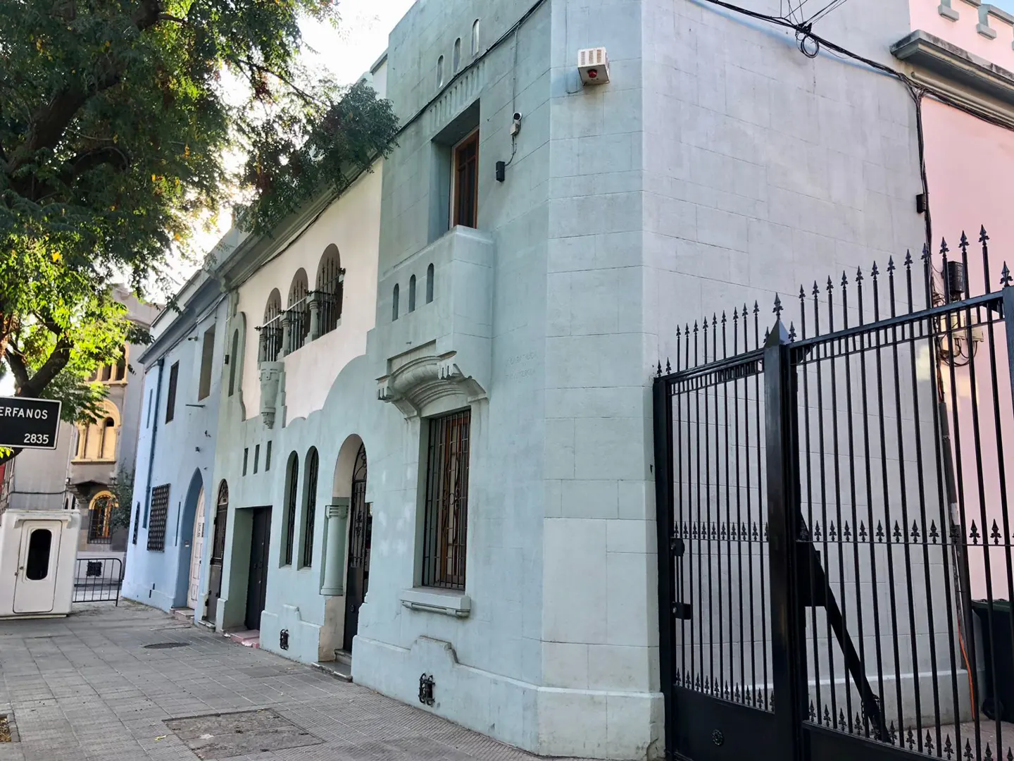 Street view of light blue and white buildings with arched windows and a black iron gate.