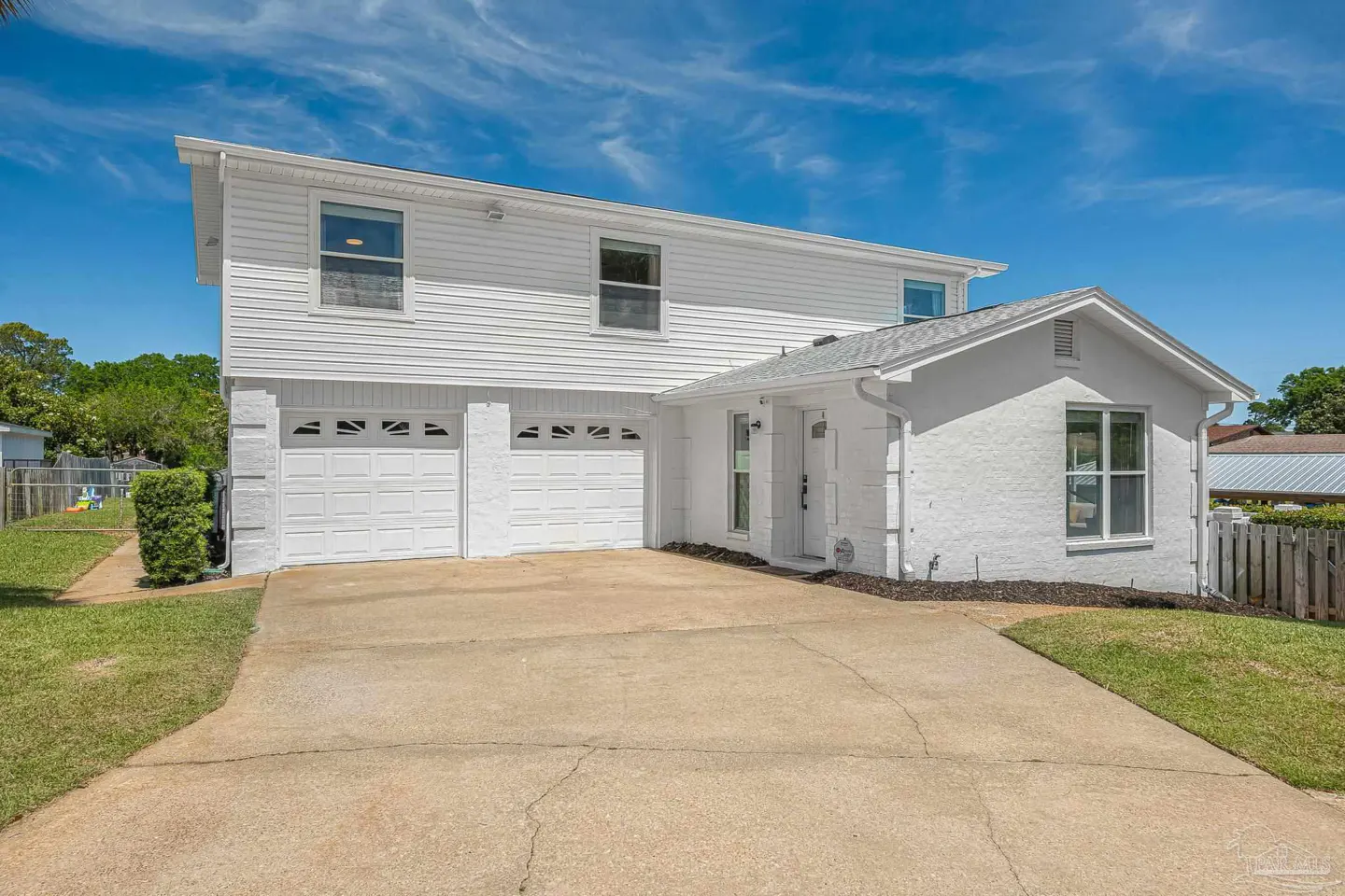 Two-story white house with a two-car garage and a concrete driveway under a blue sky.