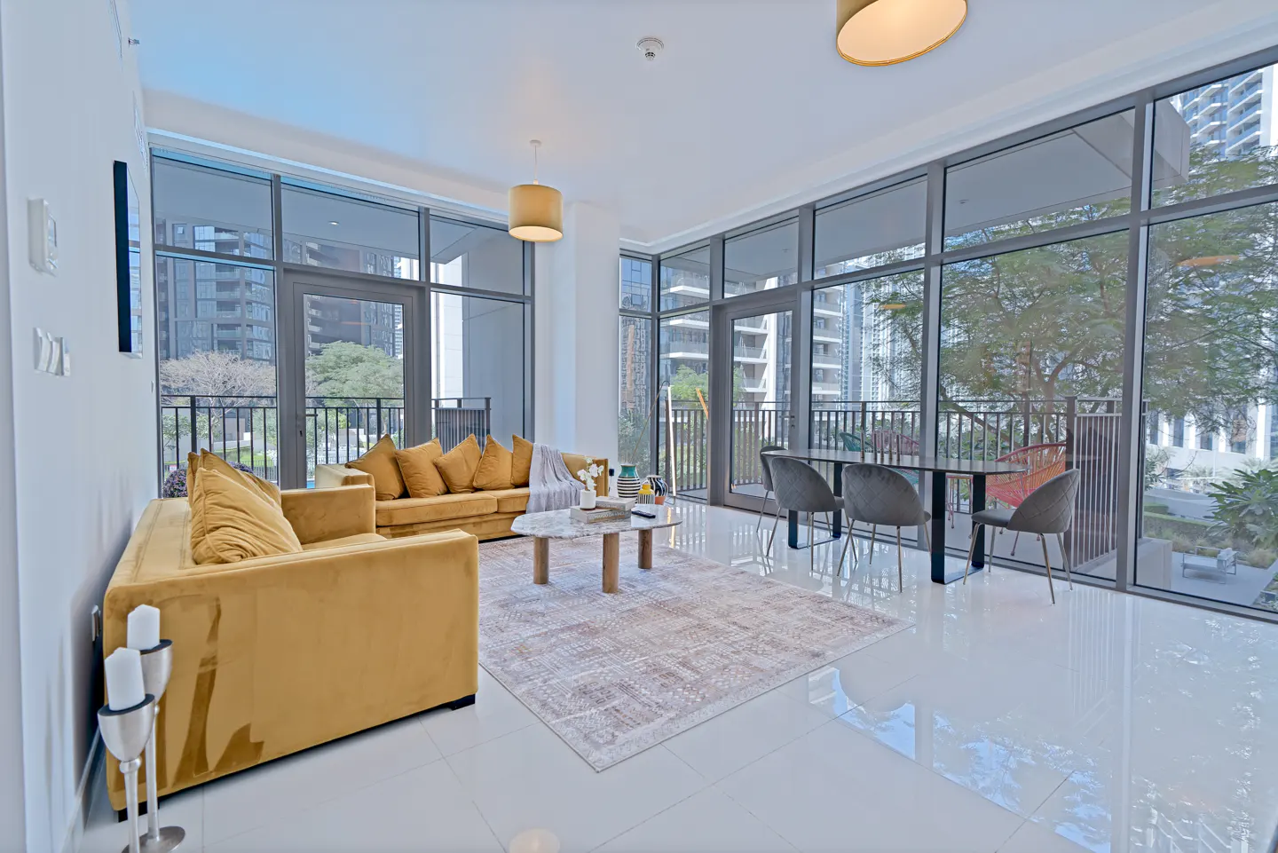 Bright living room with gold sofas, marble table, and dining set. Large windows offer city views.