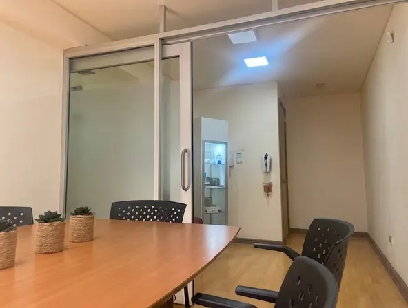 Conference room with a wood table, black chairs, and succulents. A glass sliding door leads to a hallway with a display case.