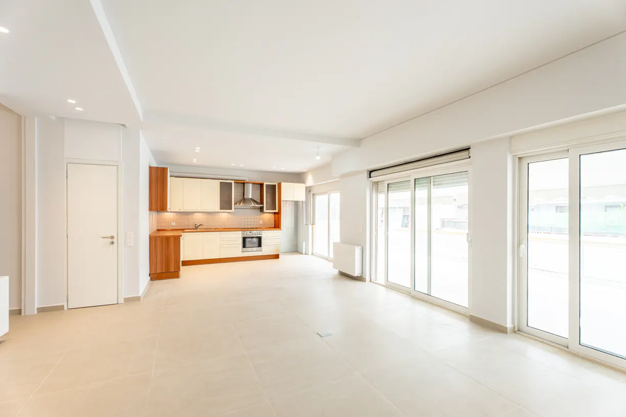 Bright, open-plan living area with beige tile floors, white walls, and a modern kitchen with wood and cream cabinets.