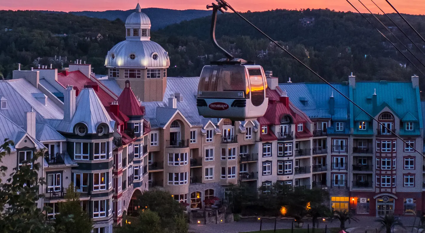 Scenic view of Mont-Tremblant resort with colorful buildings and a cable car against a sunset sky.