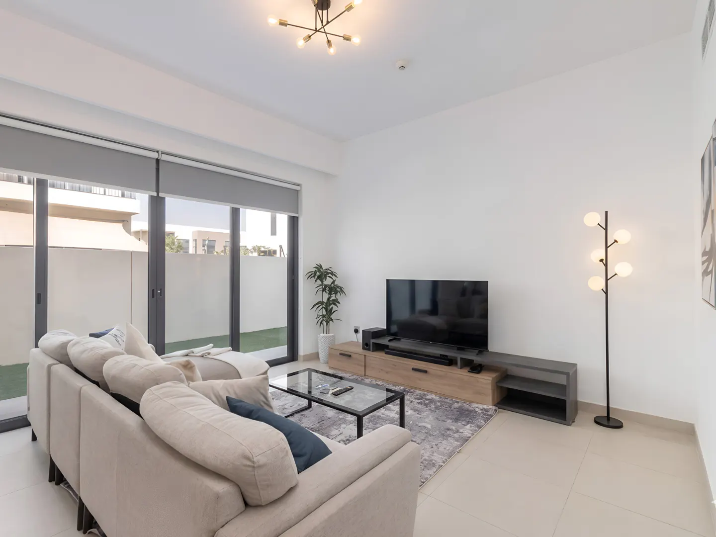 Modern living room with a beige sectional sofa, glass coffee table, TV on a wood console, and a tall floor lamp.