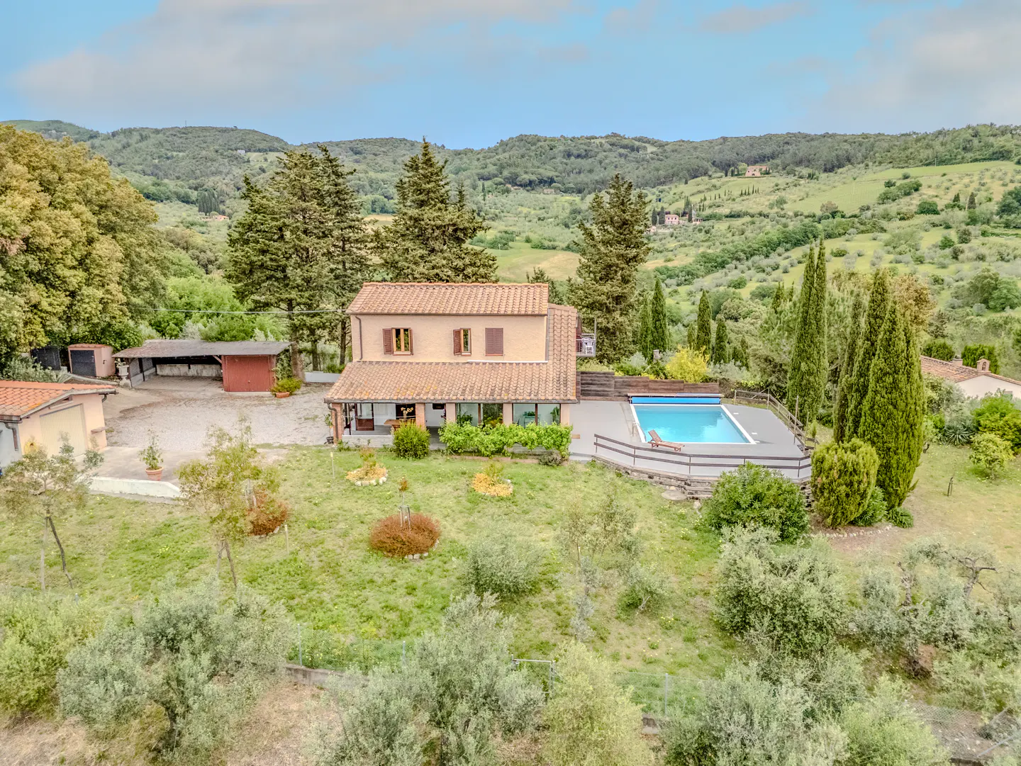 Aerial view of a two-story house with a red tile roof, a pool, and green hills in the background.