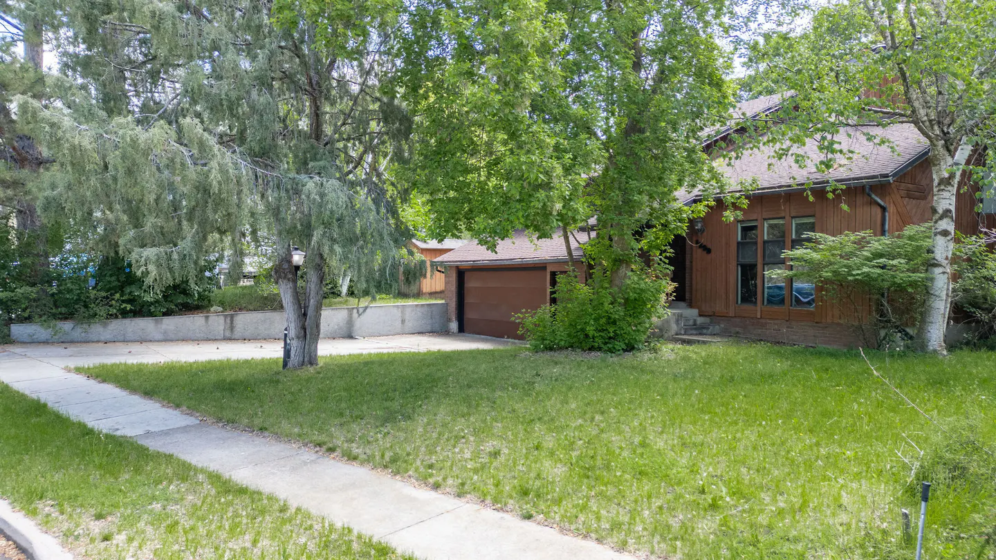 A brown house with a brown garage door is surrounded by green trees and grass.