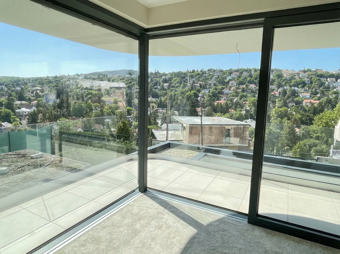 View from a modern room with large windows overlooking a green, hilly landscape with houses.