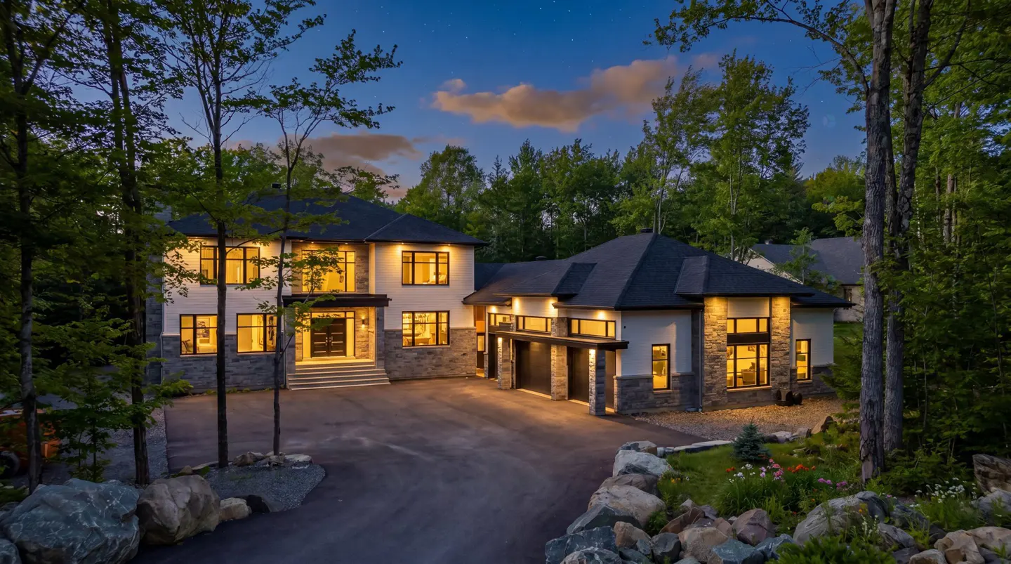 Exterior view of a modern two-story house with a black roof, stone accents, and a paved driveway at dusk.