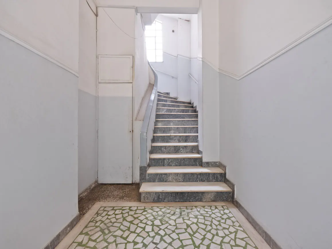 Staircase with grey marble steps, light blue walls, and a mosaic tile floor in a bright, minimalist apartment building.