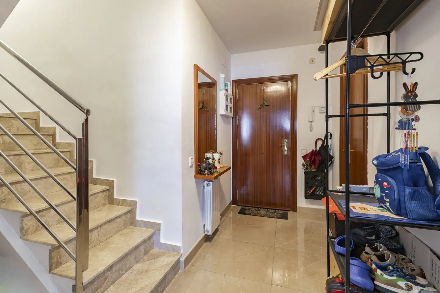 Entryway with marble stairs, a wooden front door, a wall mirror with a shelf, and a metal rack holding a blue backpack.
