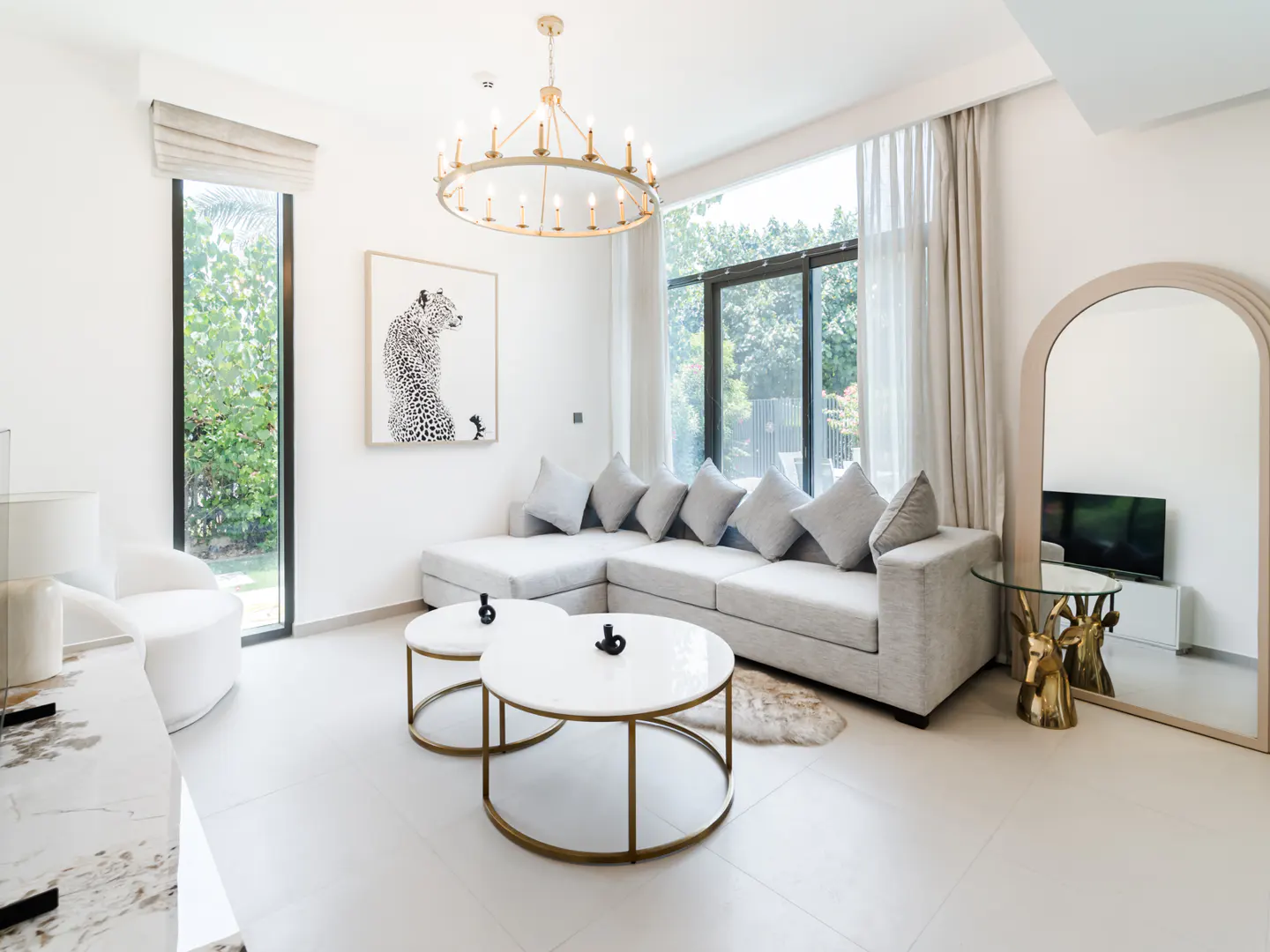 Bright modern living room with a grey sectional sofa, two round white coffee tables, and a large arched floor mirror.
