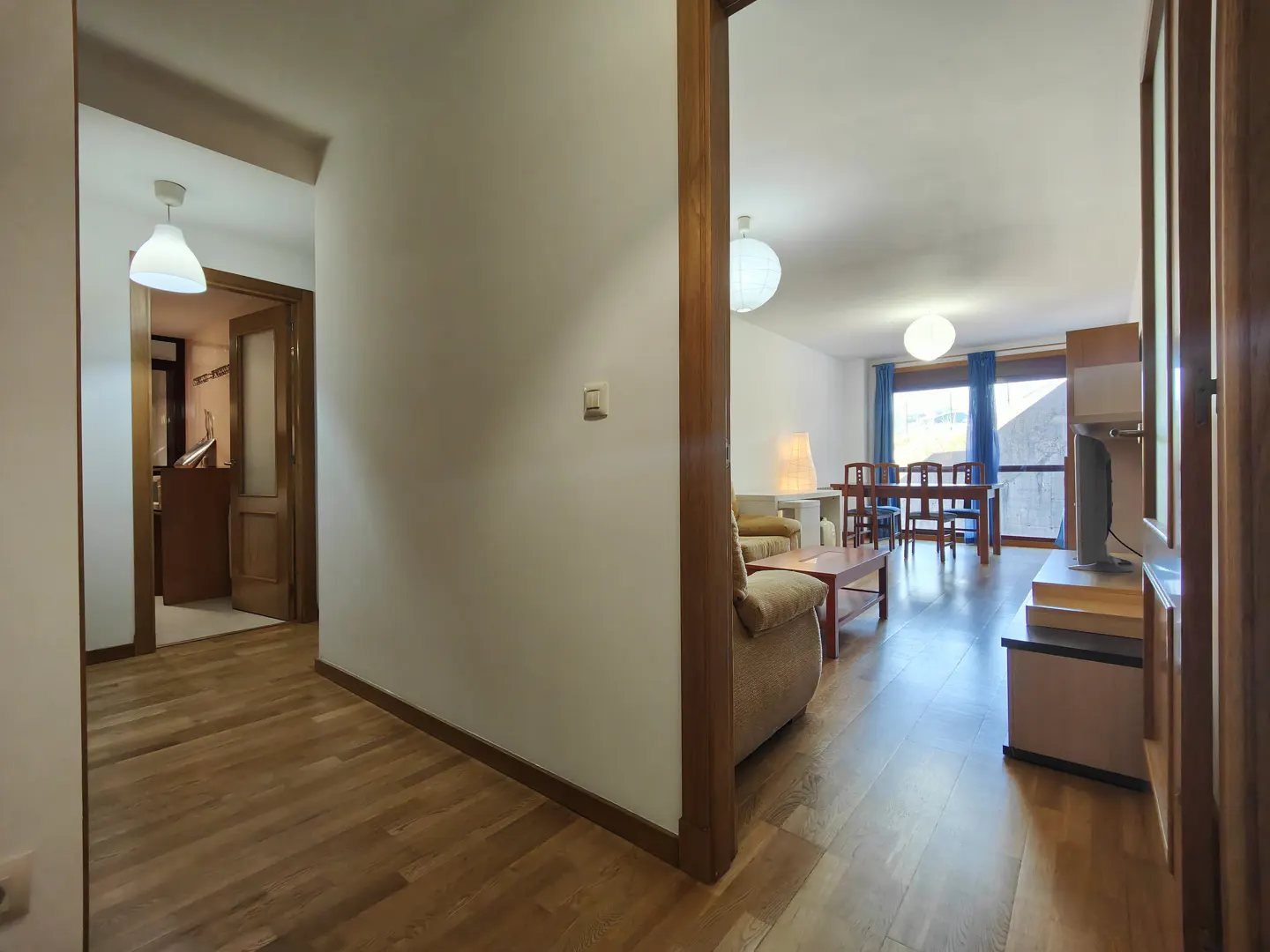Interior view of a home with hardwood floors, white walls, and a glimpse into the living room and kitchen.